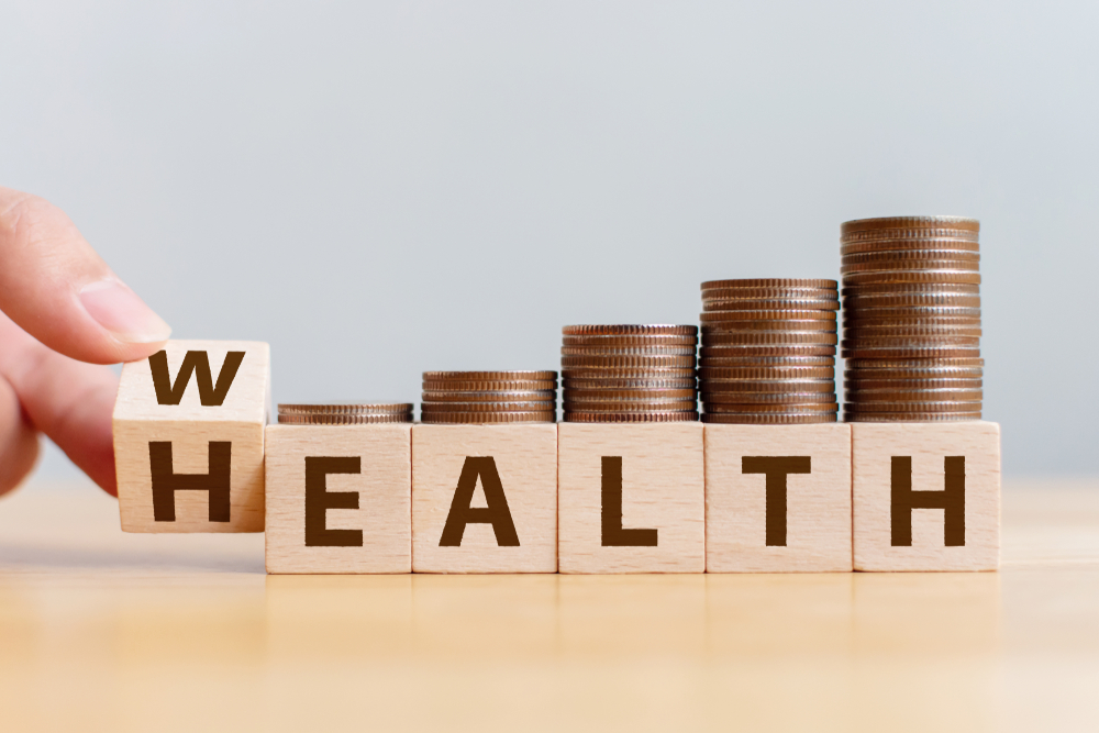 Hand flip wooden cube with word wealth to health with coins stack step up growing growth value. Investment in life insurance and healthcare concept
